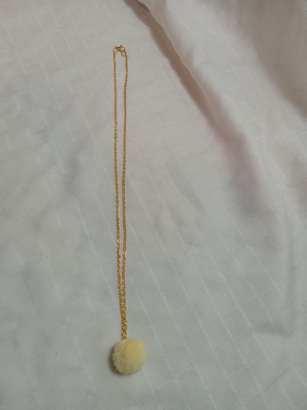 Handmade necklace with a small pom-pom and gold-colored accent hooks and chains